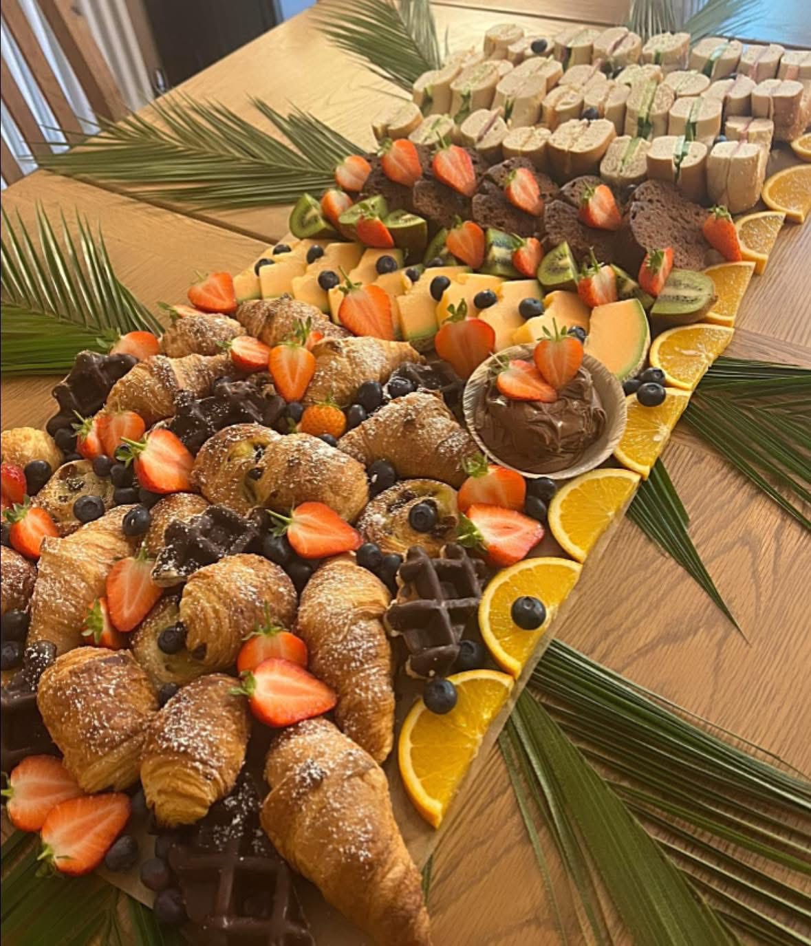 Brunch display board with croissants, waffles, strawberries and sandwiches