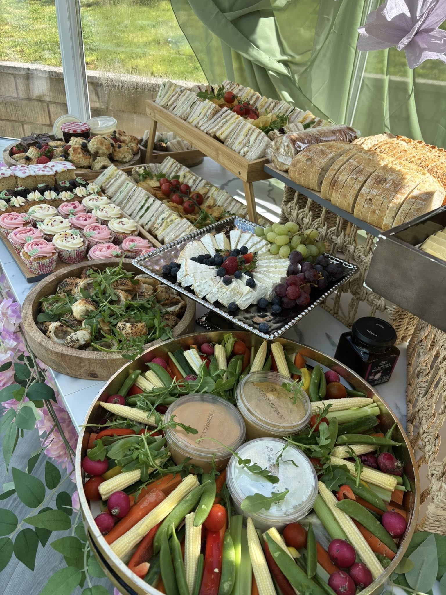 Outdoor event spread with crudités, cheese board, cupcakes and sandwiches